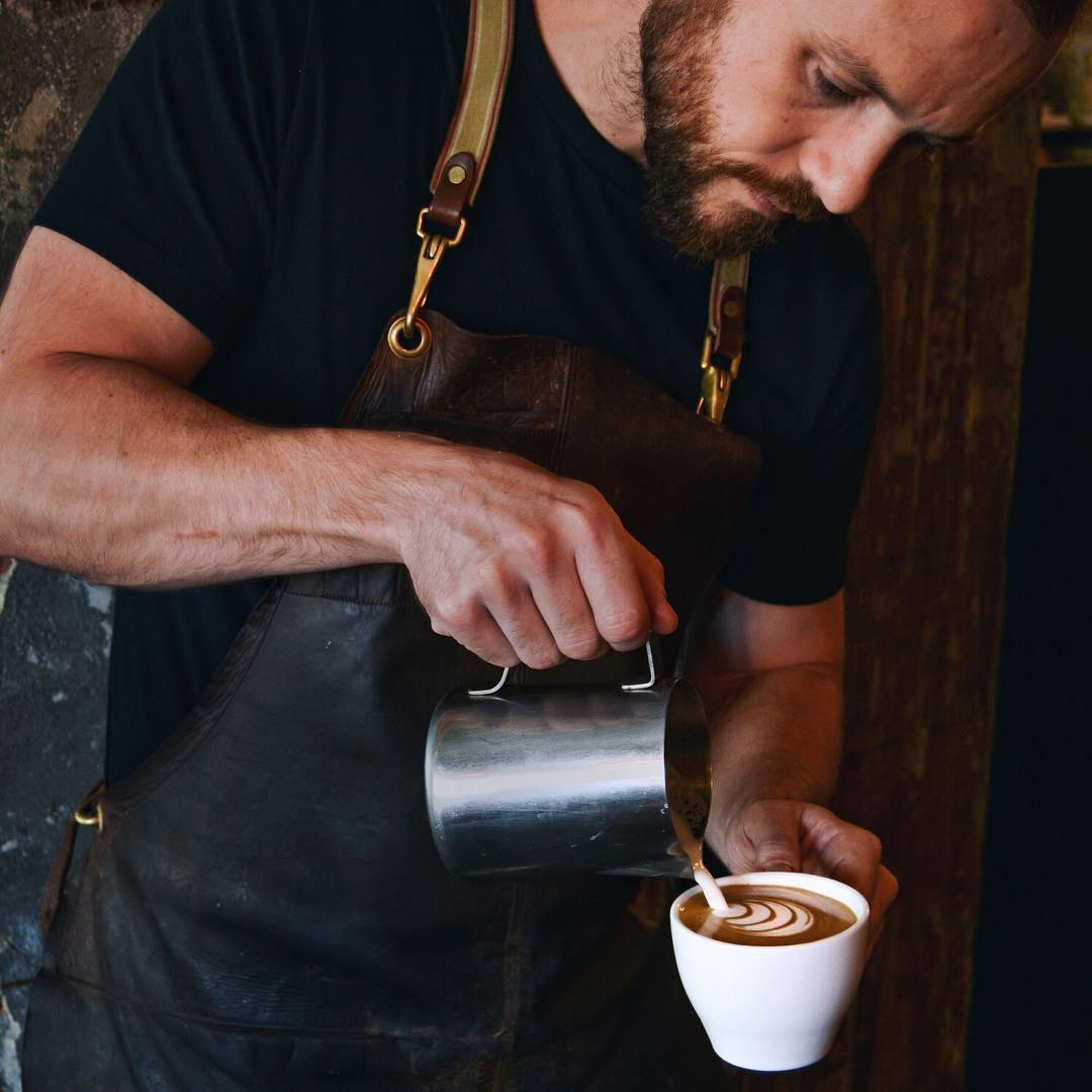 Hand pouring milk into coffee cup.