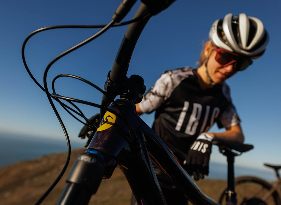 Woman poses with IBIS mountain bike featuring the bird logo and the large IBIS logo on her shirt