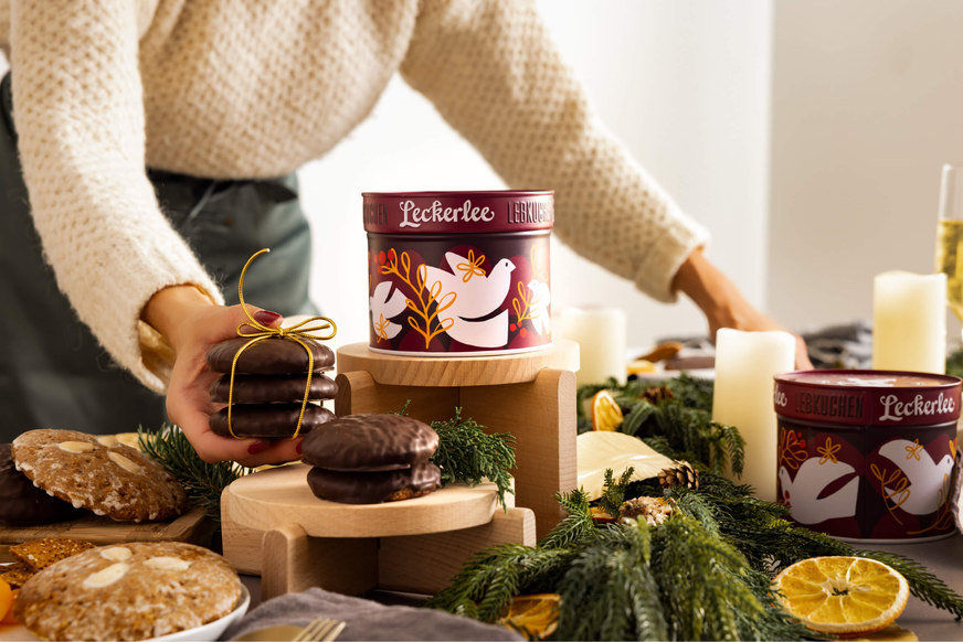 a woman sets a holiday table with german lebkuchen cookies amidst purple custom leckerlee dove tins