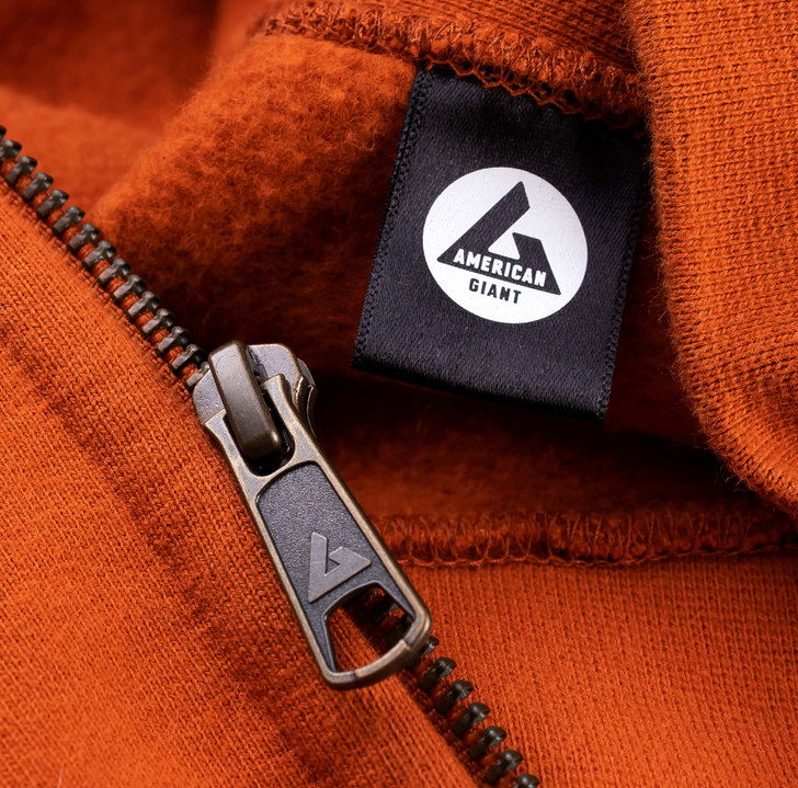 closeup image of an American Giant sweatshirt featuring a customized zipper with embossed logo as well as a customized neck tag with the A monogram logo